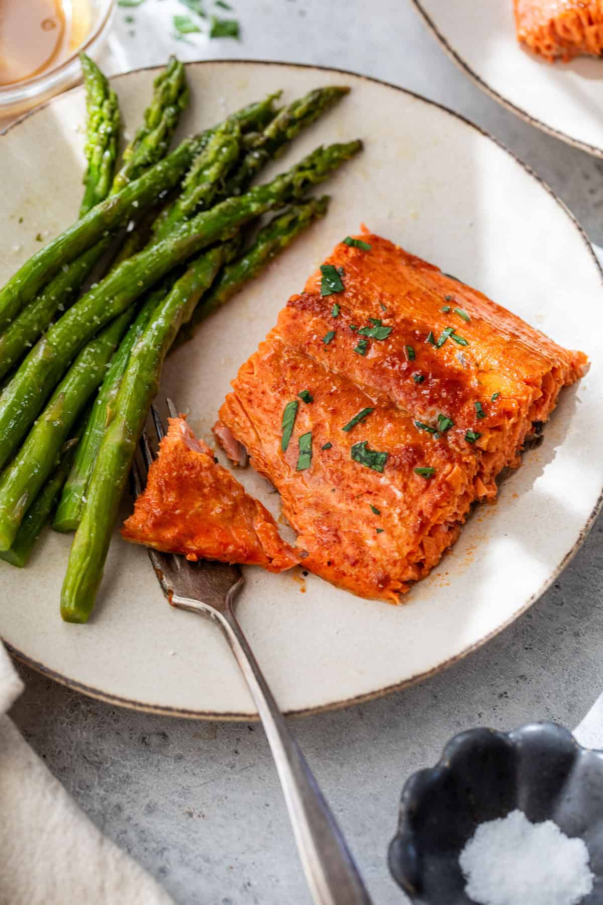 A plate with honey mustard salmon fillet, cooked asparagus, and a fork holding a bite of salmon.