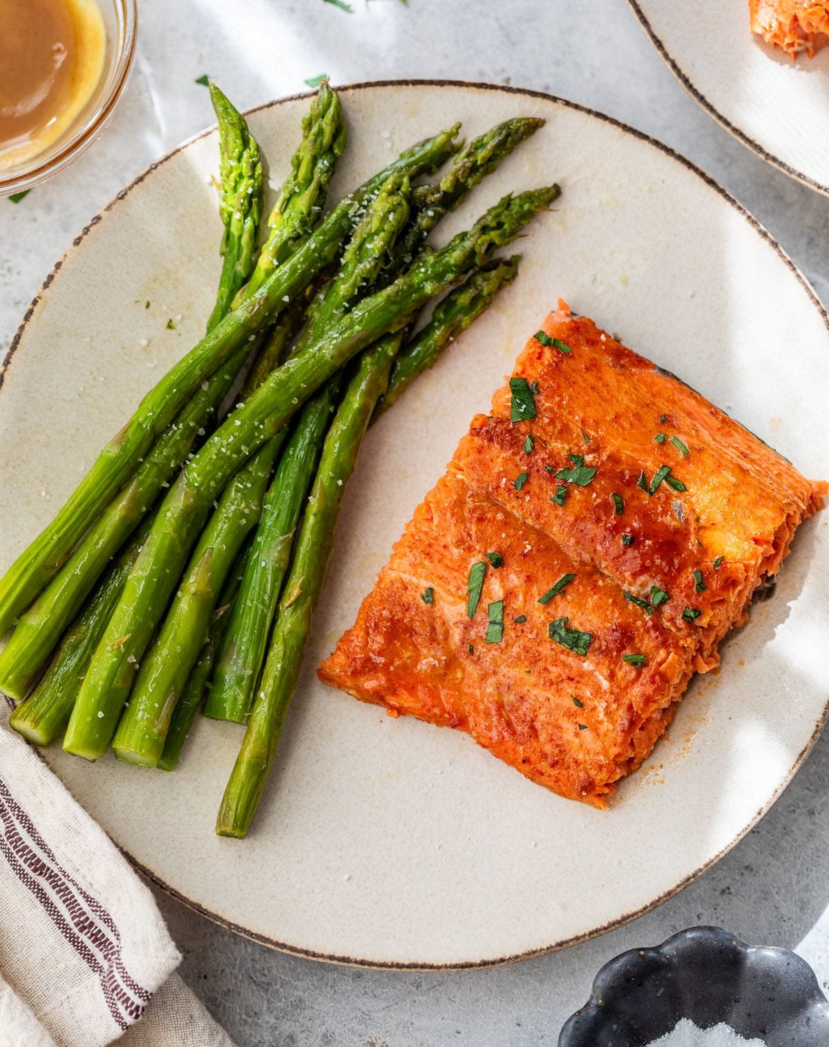 A plate with honey mustard salmon and steamed asparagus, garnished with herbs, on a light background.