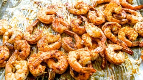 Seasoned, roasted shrimp spread out on a baking sheet lined with parchment paper.