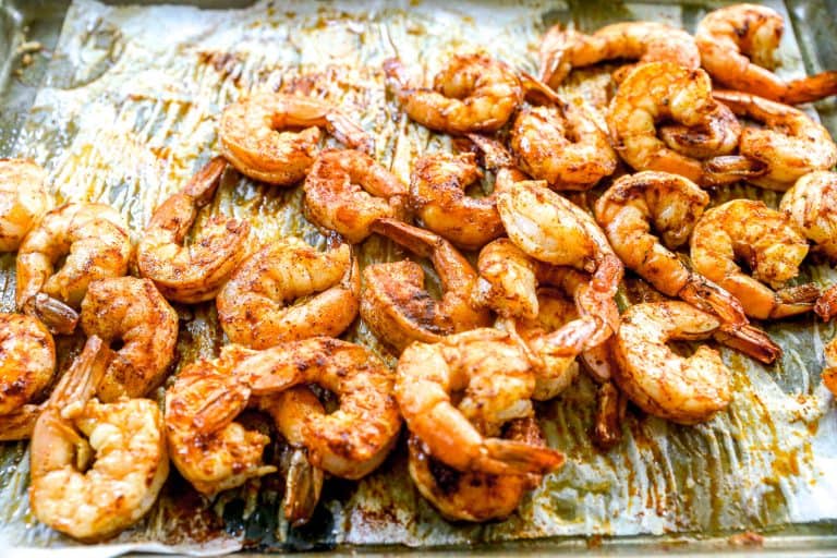 Seasoned, roasted shrimp spread out on a baking sheet lined with parchment paper.