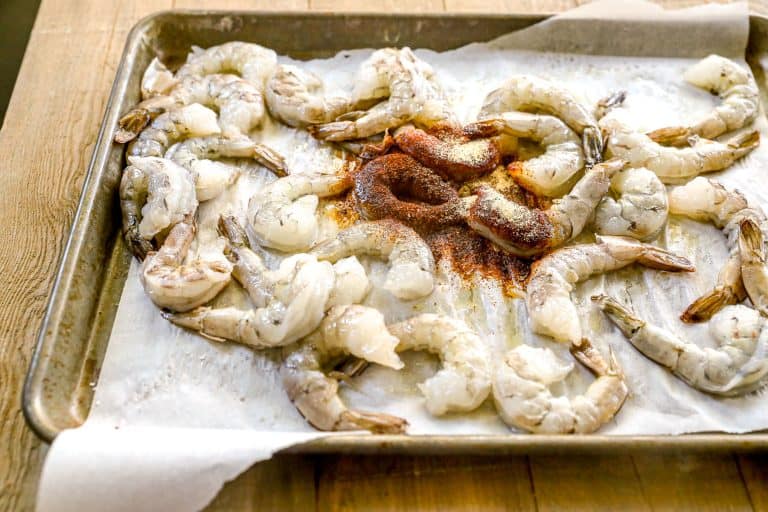 Raw shrimp arranged on a parchment-lined baking sheet with spices sprinkled in the center.