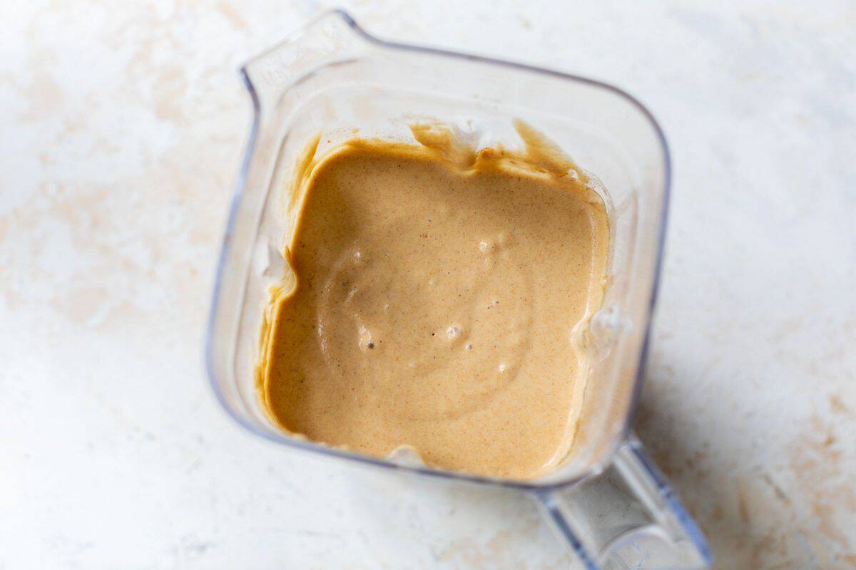 Thick healthy waffle batter inside a transparent blender jar on a light-colored surface.