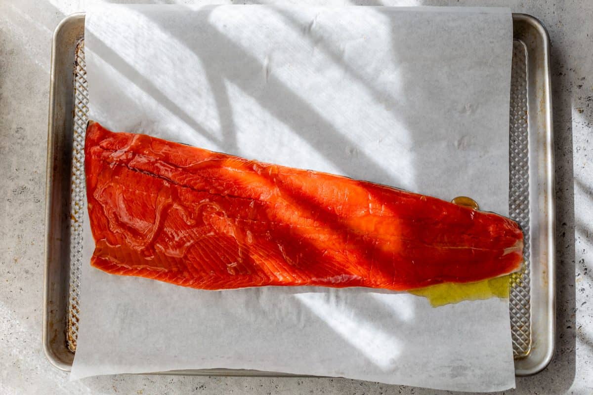 A raw salmon fillet on parchment paper atop a baking sheet, with sunlight casting shadows across it.