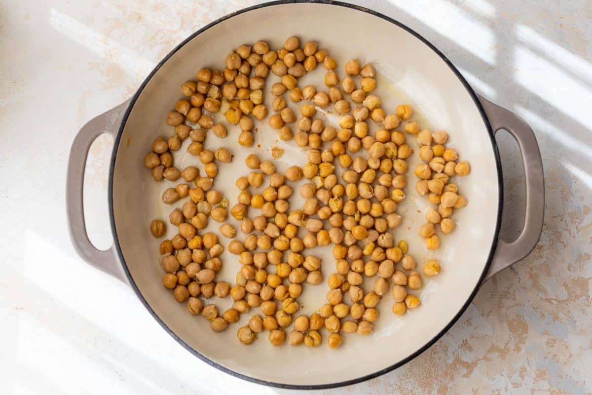 Chickpeas scattered in a large, light-colored pan with handles, placed on a white surface in sunlight.