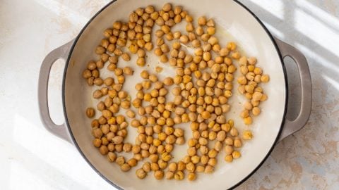 Chickpeas scattered in a large, light-colored pan with handles, placed on a white surface in sunlight.