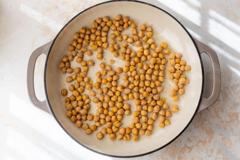 Chickpeas scattered in a large, light-colored pan with handles, placed on a white surface in sunlight.