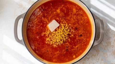 A pot of pasta e ceci with dry ditalini pasta and a parmesan rind on top, before stirring.