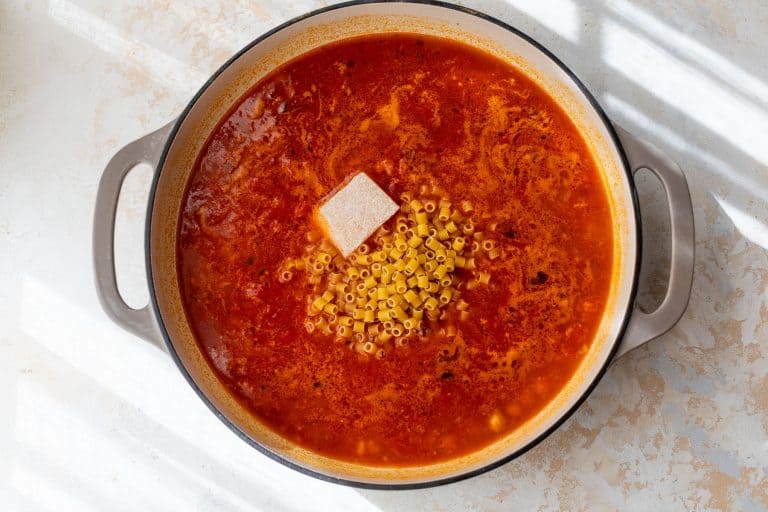 A pot of pasta e ceci with dry ditalini pasta and a parmesan rind on top, before stirring.