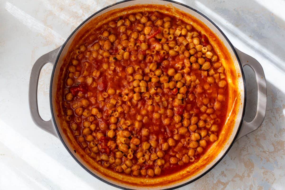 A large pot filled with pasta a ceci in tomato broth, seen from above on a light surface.