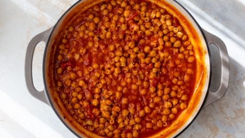 A large pot filled with pasta a ceci in tomato broth, seen from above on a light surface.