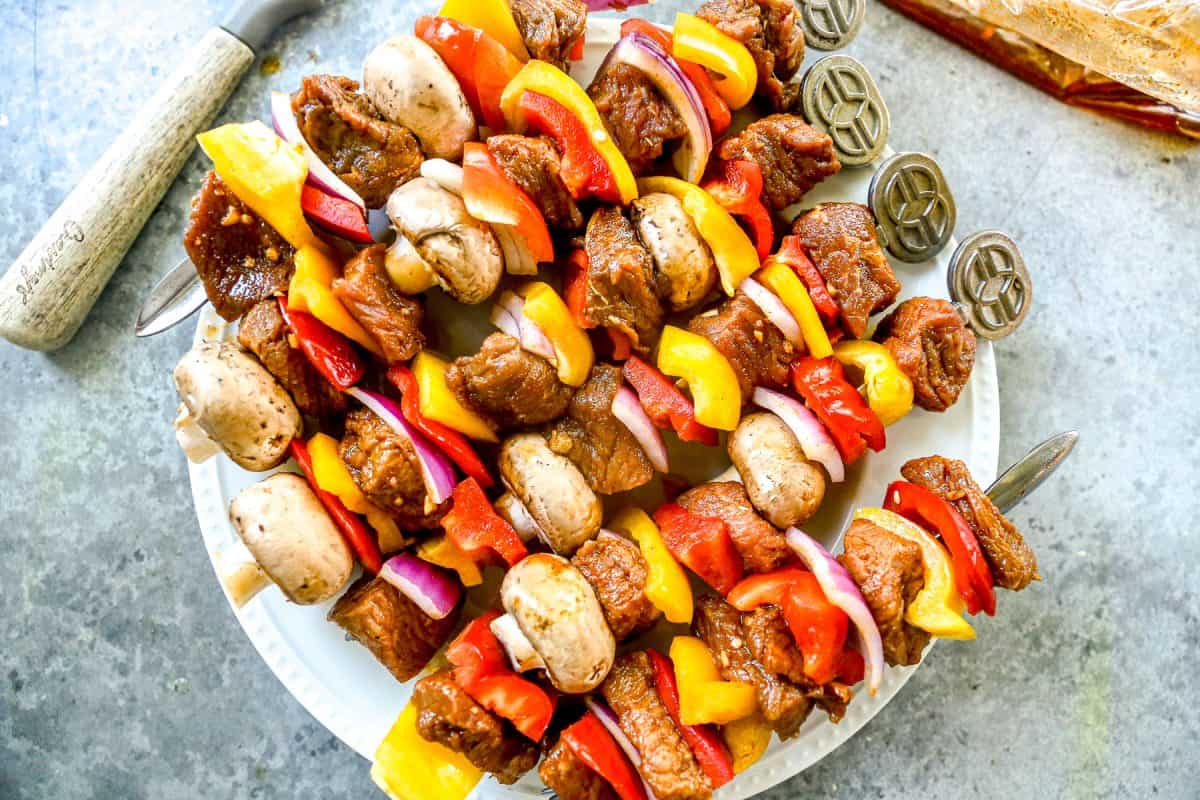 Kabobs with marinated steak, mushrooms, bell peppers, and onions arranged on a white plate.