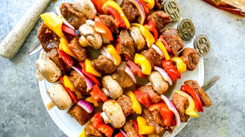 Kabobs with marinated steak, mushrooms, bell peppers, and onions arranged on a white plate.