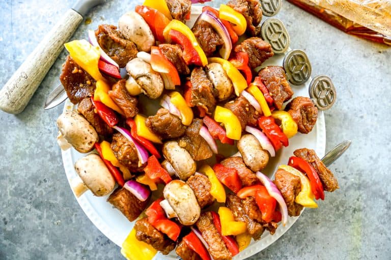 Kabobs with marinated steak, mushrooms, bell peppers, and onions arranged on a white plate.