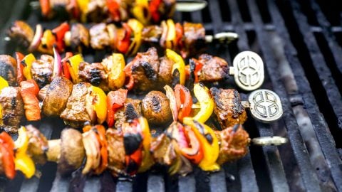 Skewers of grilled steak and colorful vegetables cooking on a barbecue grill.