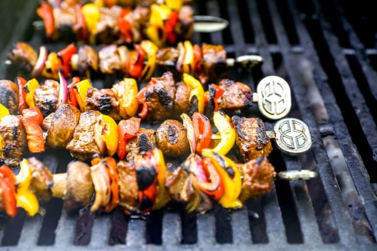 Skewers of grilled steak and colorful vegetables cooking on a barbecue grill.