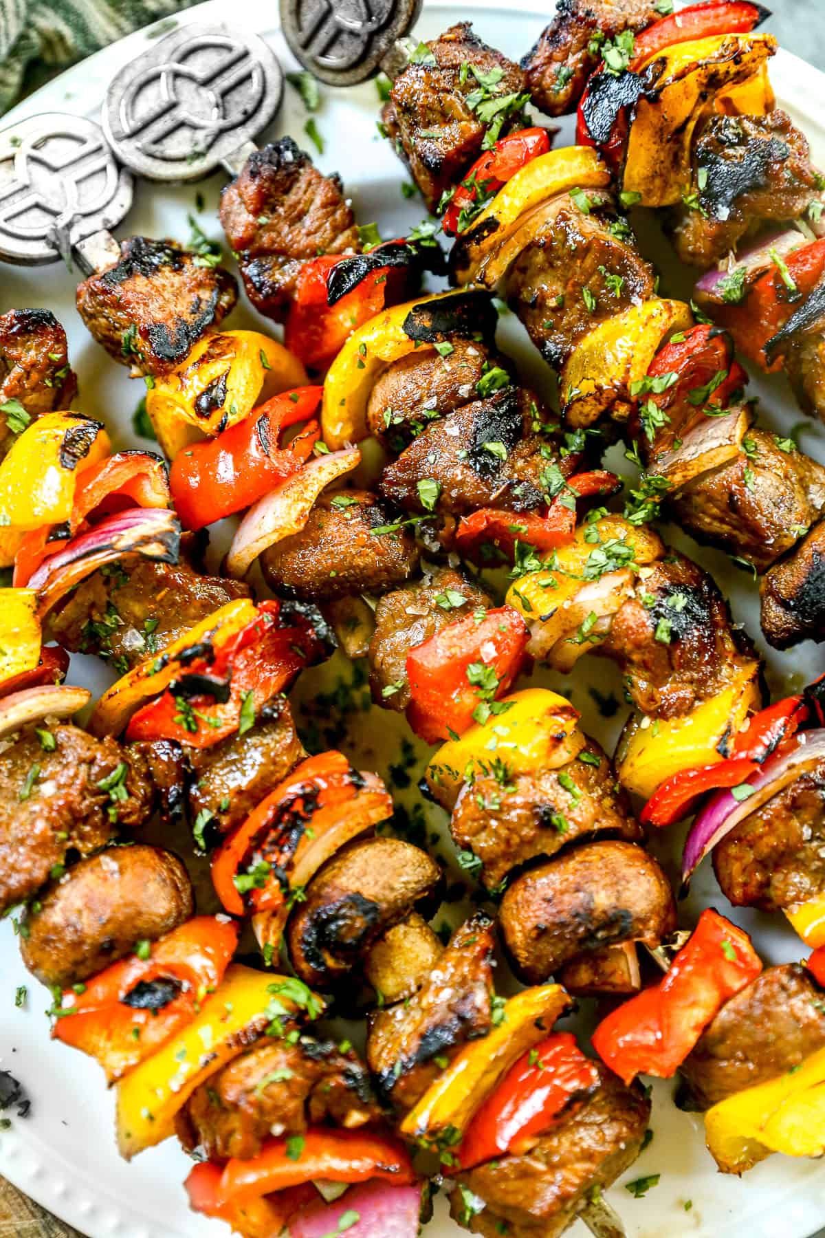 Grilled steak kabobs with peppers and onions, garnished with chopped herbs on a white plate.