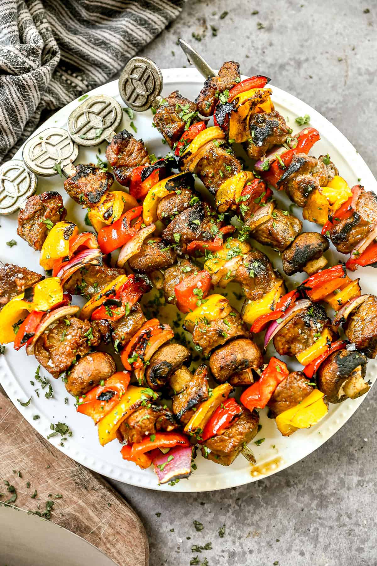 Grilled steak kabobs on skewers, served on a white plate with herbs sprinkled on top.