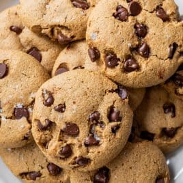 A plate of chocolate chip almond flour cookies stacked on top of each other on a white surface.