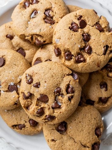 A plate of chocolate chip almond flour cookies stacked on top of each other on a white surface.