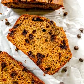 Sliced chocolate chip zucchini bread on parchment paper with chocolate chips scattered around.