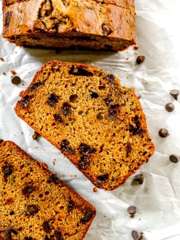 Sliced chocolate chip zucchini bread on parchment paper with chocolate chips scattered around.