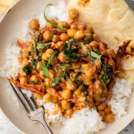 Chickpea curry with spinach and tomatoes served over white rice, with naan bread on the side in a bowl.