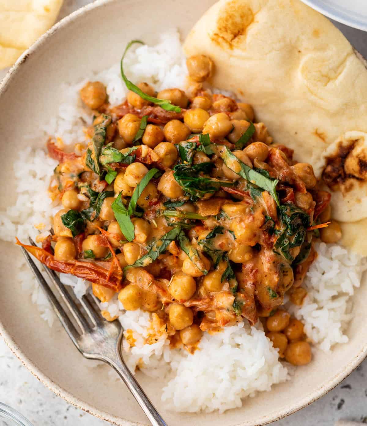Chickpea curry with spinach and tomatoes served over white rice, with naan bread on the side in a bowl.