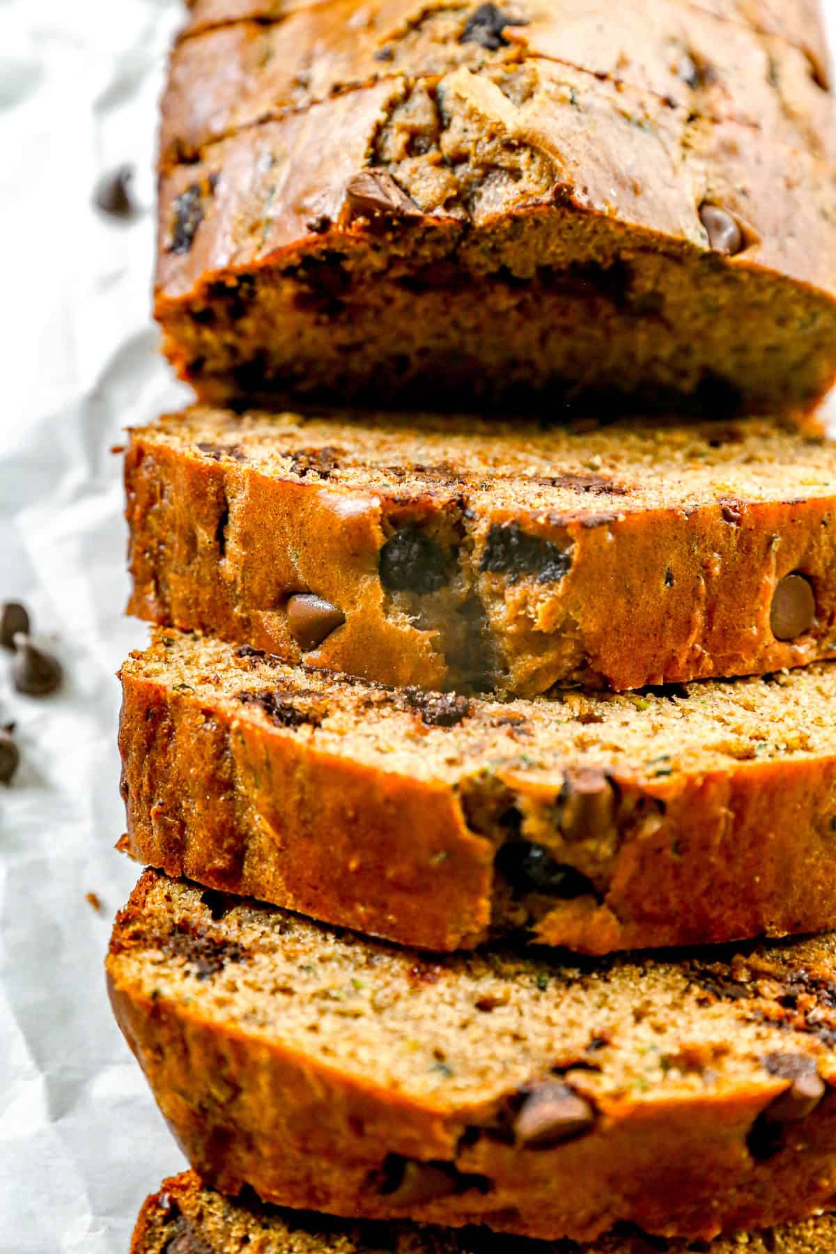 Sliced chocolate chip zucchini bread on a white surface, showing moist texture and chocolate chips inside.