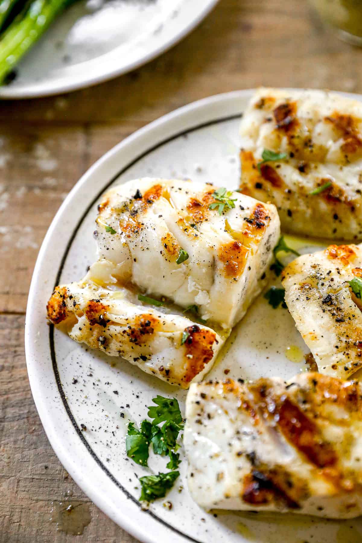 Keep things light and fresh with this easy Grilled Cod! It's a healthy, quick dinner that everyone will enjoy! Grilled cod fillets on a white plate, garnished with chopped herbs and cracked black pepper.