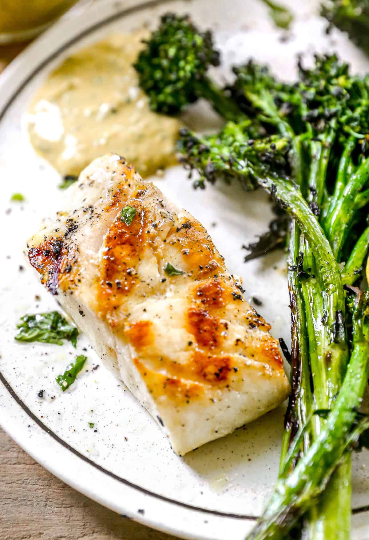 Bright flavors are packed into every bite of this easy Grilled Cod with cilantro yogurt sauce! It's a healthy dish to serve for quick weeknight meals or parties! Grilled cod fillet served with broccolini and a dollop of creamy sauce on a white plate.