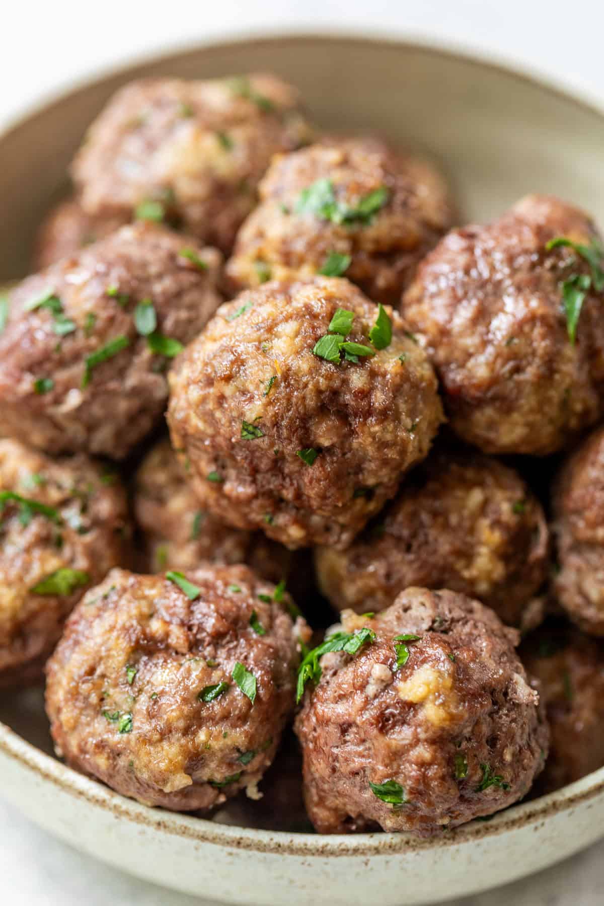 A bowl filled with homemade ground beef meatballs garnished with chopped fresh herbs.