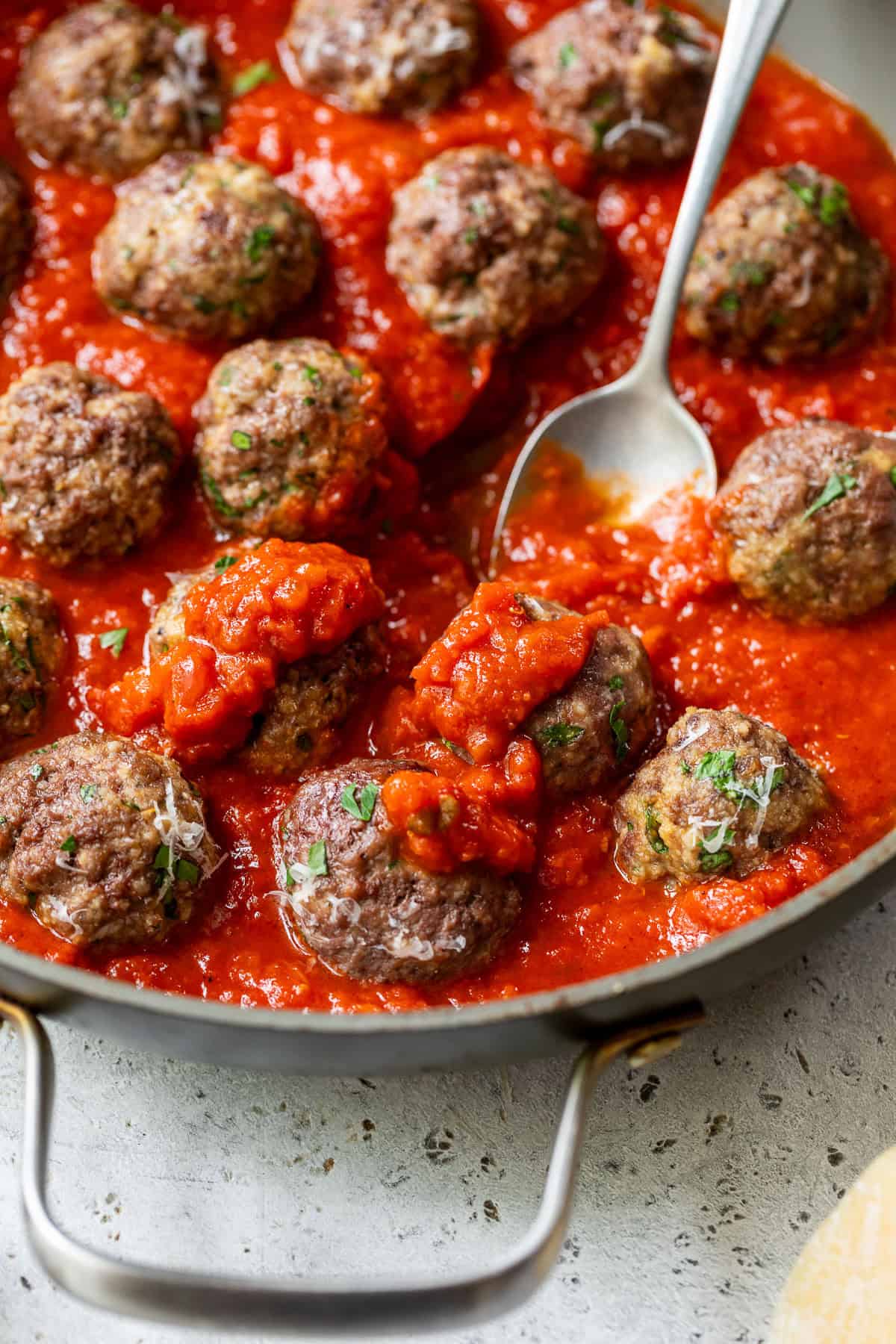 Ground beef meatballs in tomato sauce in a skillet, with a spoon scooping up meatballs and sauce.