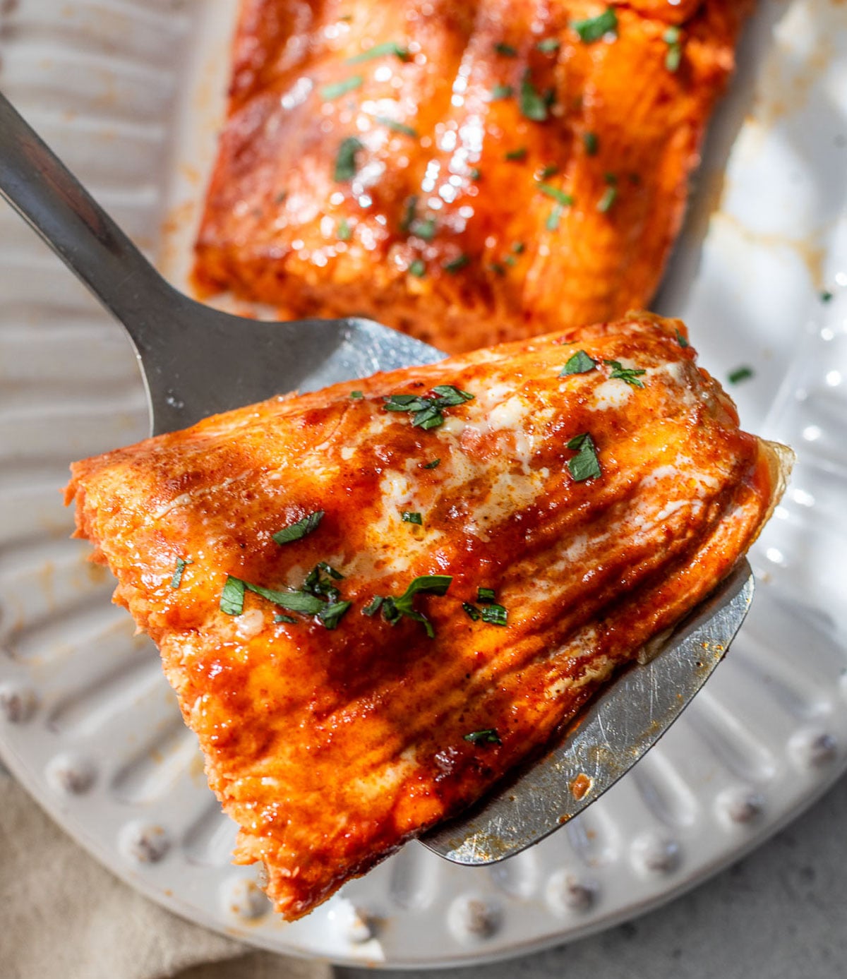 A fork holds a glazed honey mustard salmon fillet topped with chopped herbs