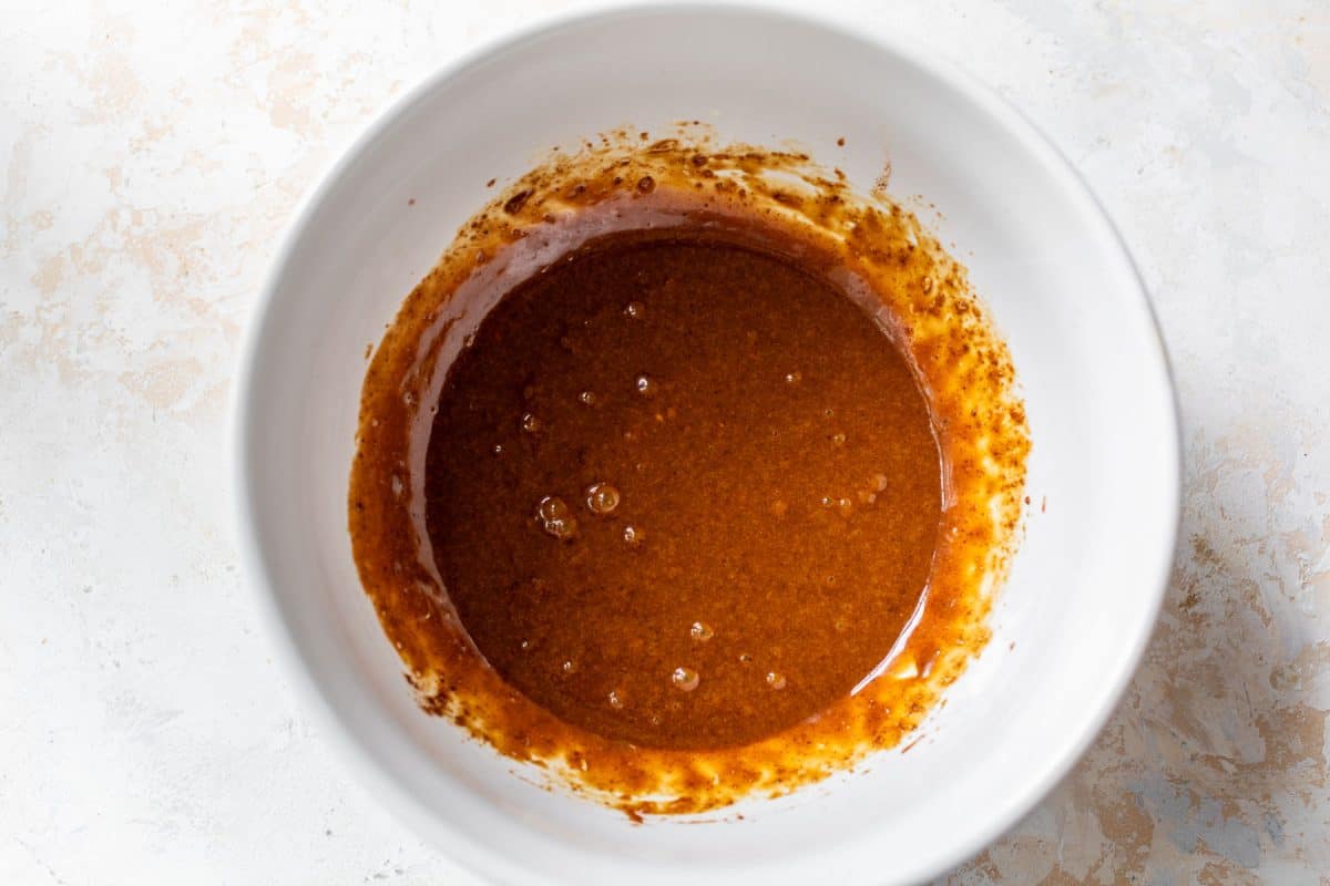Wet ingredients for cookies with bubbles in a white bowl, set on a light, textured surface.