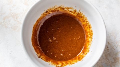 Wet ingredients for cookies with bubbles in a white bowl, set on a light, textured surface.