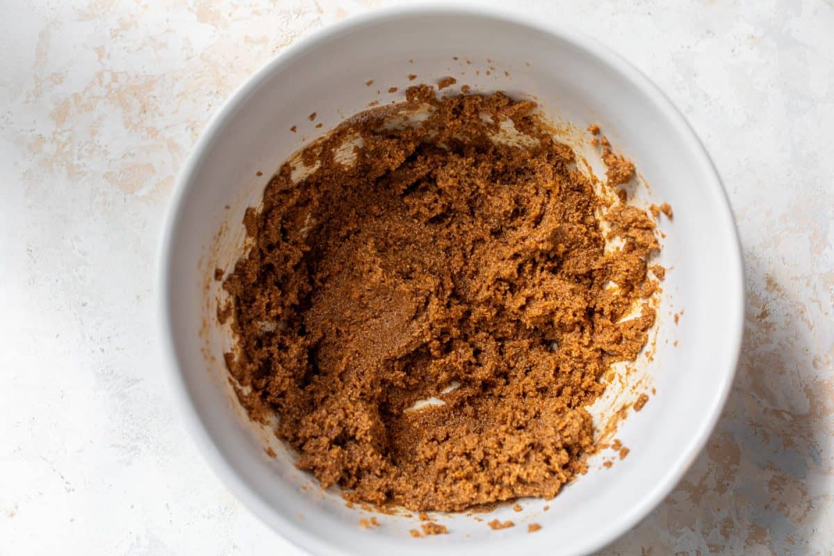 Brown sugar and butter mixture in a white bowl on a light surface, ready for baking or cooking preparation.