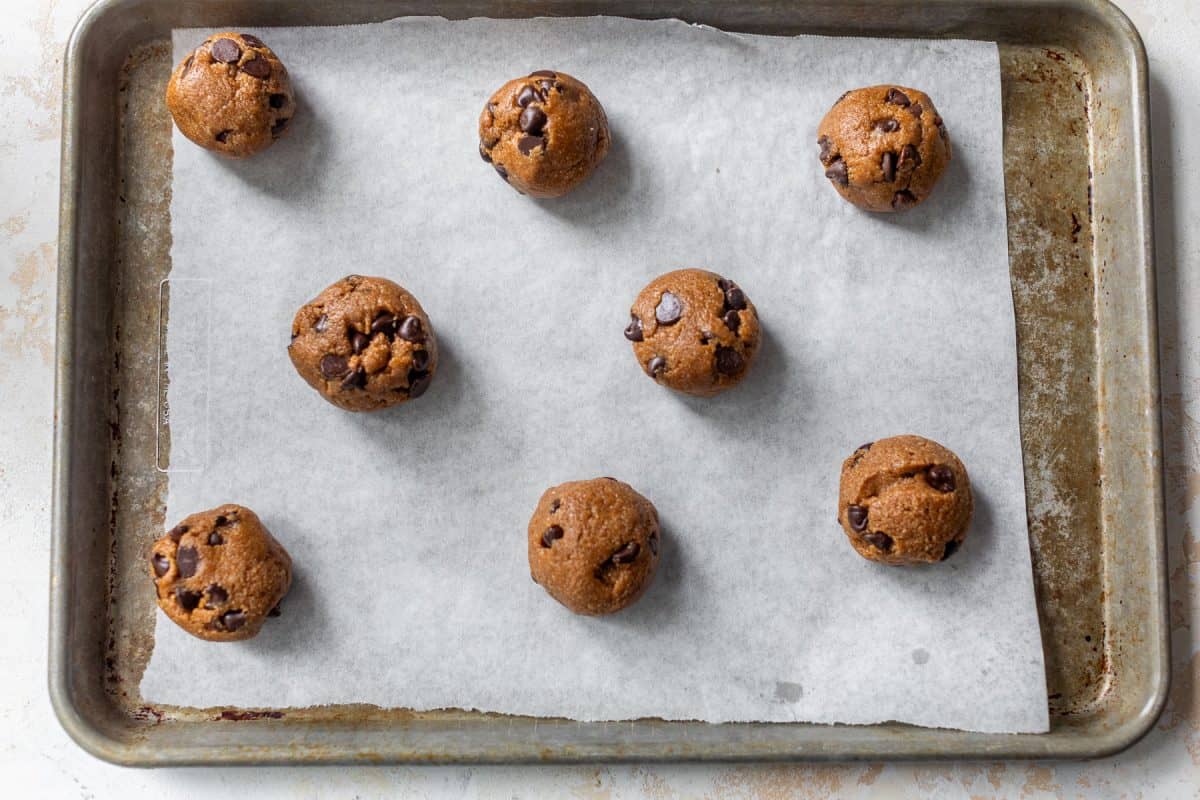 Eight chocolate chip almond flour cookie dough balls on parchment paper lined baking sheet, ready to be baked.