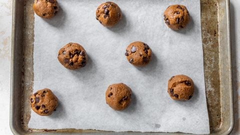 Eight chocolate chip almond flour cookie dough balls on parchment paper lined baking sheet, ready to be baked.