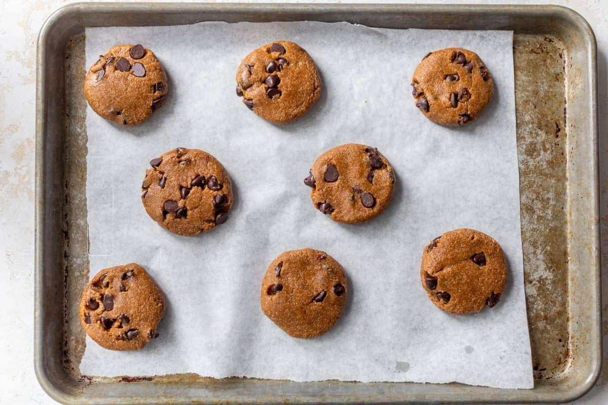 Eight unbaked chocolate chip almond flour cookie dough balls on a parchment-lined baking sheet.