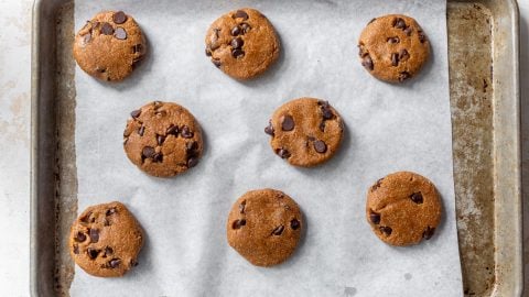 Eight unbaked chocolate chip almond flour cookie dough balls on a parchment-lined baking sheet.