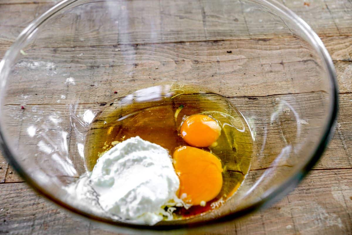 Two raw eggs and a dollop of white yogurt in a clear glass bowl on a wooden surface.