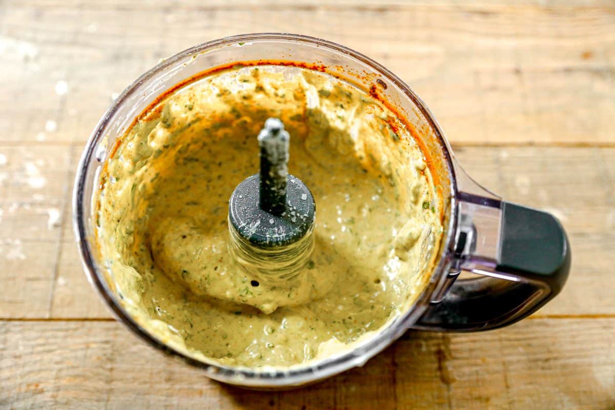A food processor with creamy green sauce inside, sitting on a wooden surface.