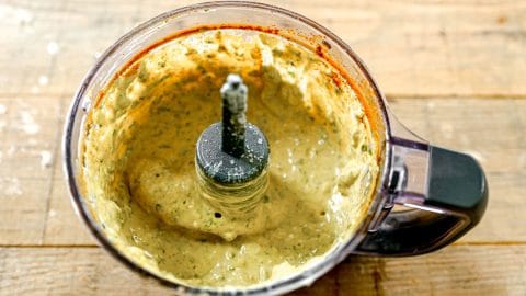A food processor with creamy green sauce inside, sitting on a wooden surface.