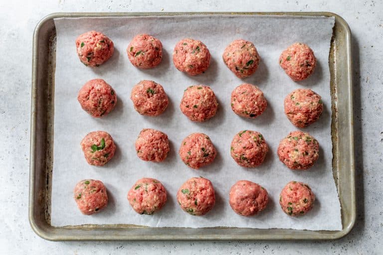 Uncooked ground beef meatballs arranged in rows on a parchment-lined baking sheet.