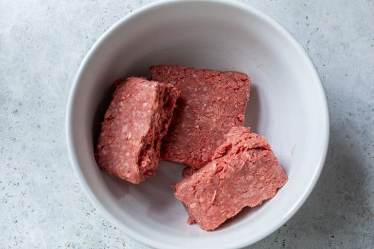 Three rectangular chunks of raw ground beef in a white bowl on a light gray countertop.