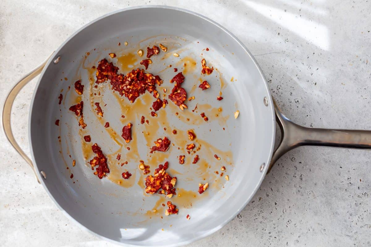 A gray frying pan with bits of cooked red chili and oil residue on a light countertop.