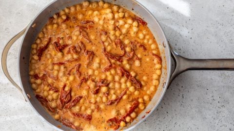 Creamy chickpea stew with sun-dried tomatoes in a skillet on a light countertop, seen from above.