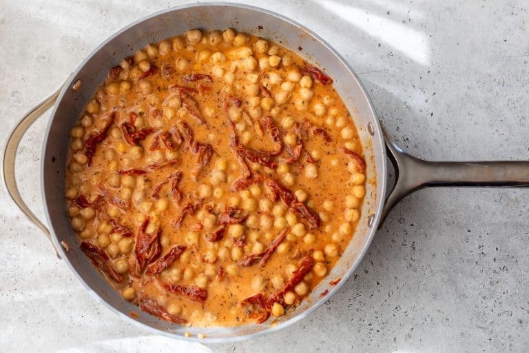Creamy chickpea stew with sun-dried tomatoes in a skillet on a light countertop, seen from above.