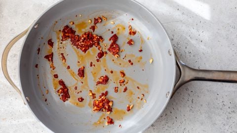 A gray frying pan with bits of cooked red chili and oil residue on a light countertop.