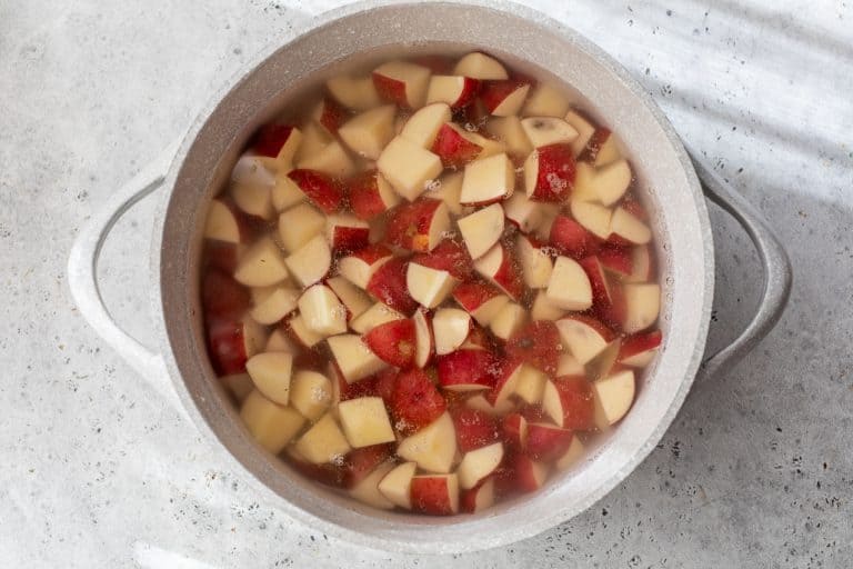 Diced red potatoes in a pot of water, ready to be boiled, on a light gray countertop.